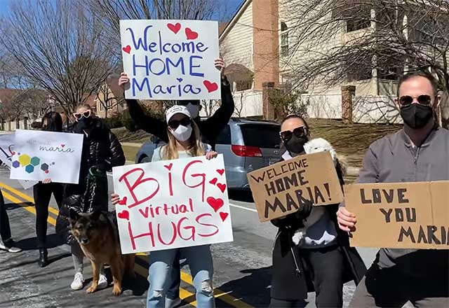 Maria's family and friends holding signs, welcoming her home