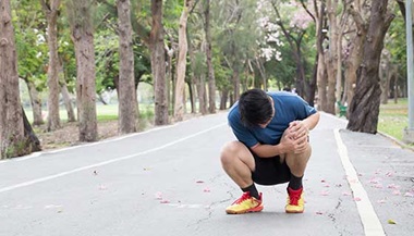 Runner crouched holding knee on running path