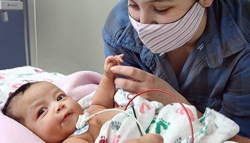 An infant in hospital bed being watched by a parent