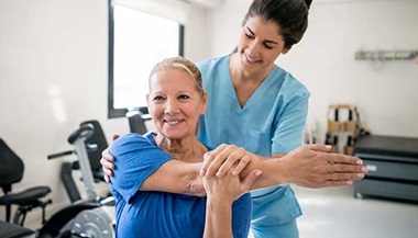 Physical therapist holding senior patient while she stretches her shoulder