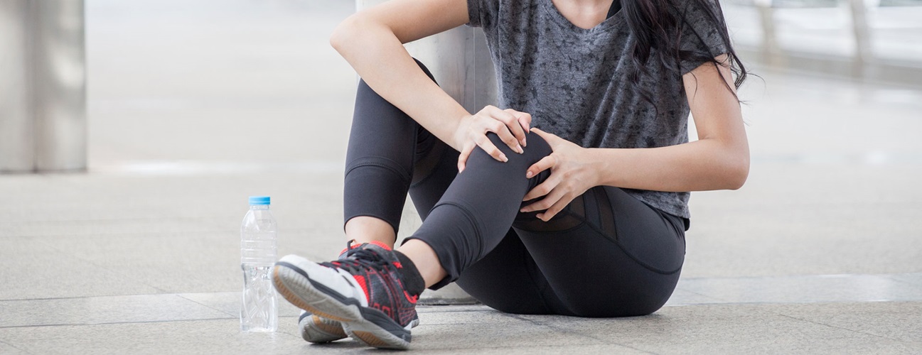 a runner sits on the ground and clutches her knee