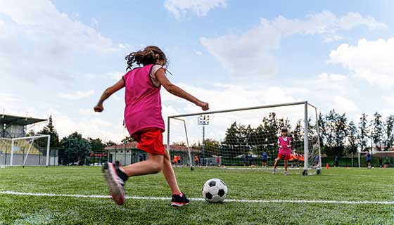 girl kicking soccer ball into goal