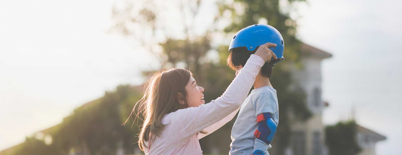 Mom strapping a biking helmet onto her child's head.