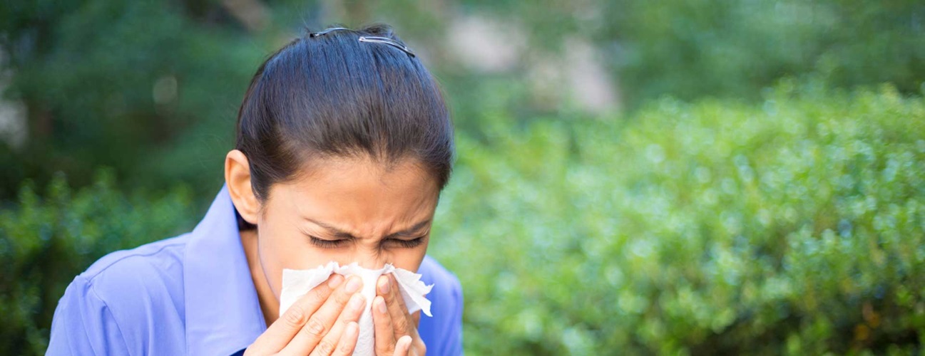 woman sneezing around bushes outside